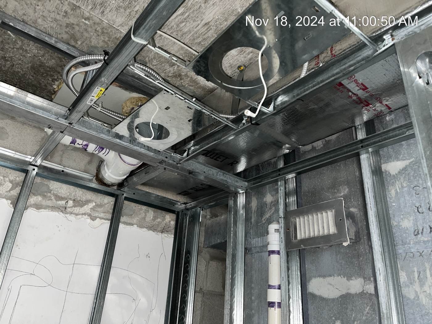 Interior construction in progress — metal stud framing, ceiling grid and overhead ductwork.